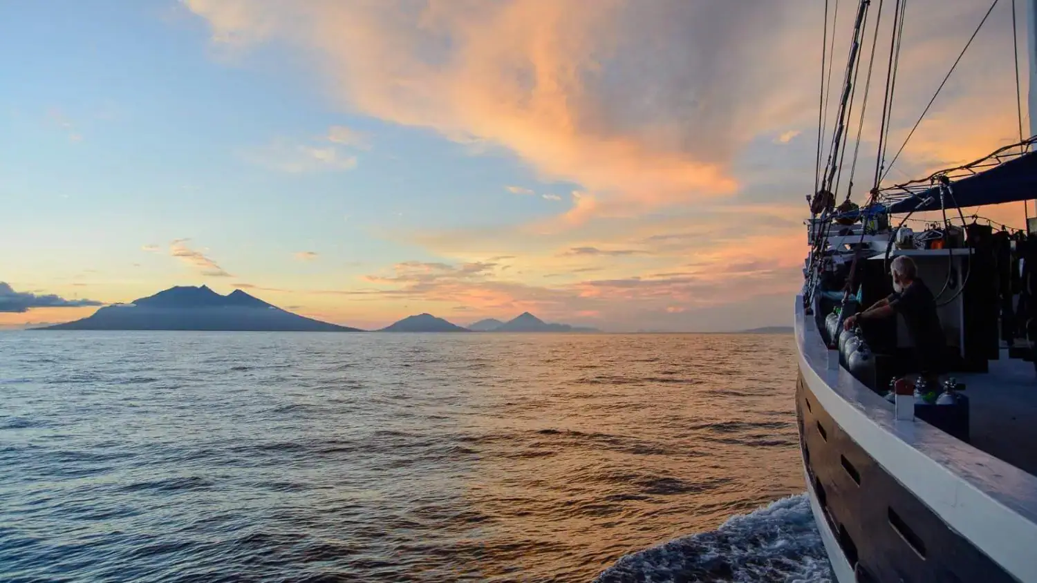 boat sailing, sunset, island silhouette, golden sky, calm ocean, tropical journey