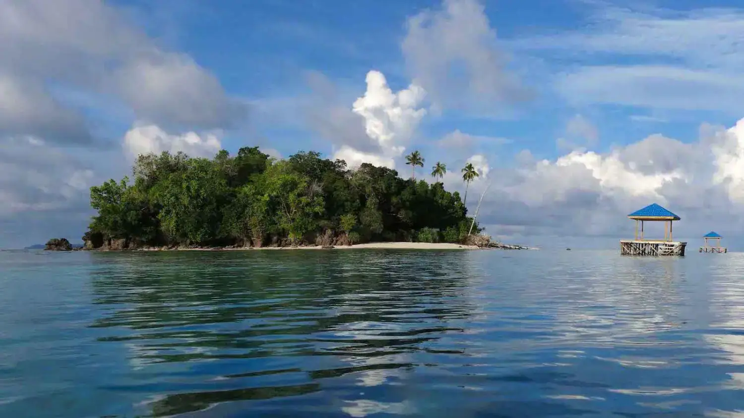 tiny island, remote location, clear water, blue sky, lush greenery, white sand beach