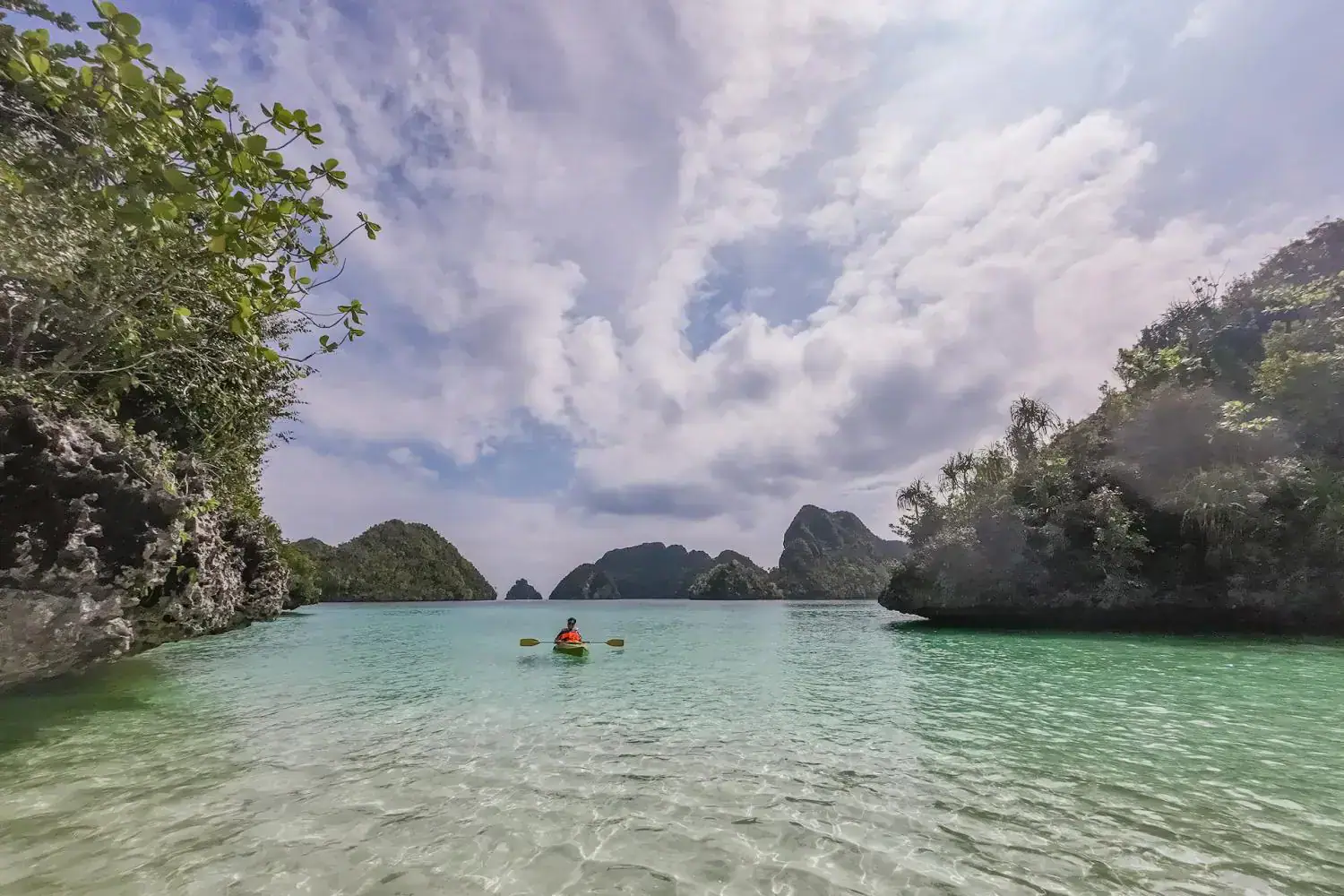 kayaking with view, green hills all around, cloudy sky, crystal clear water surrounding kayaks