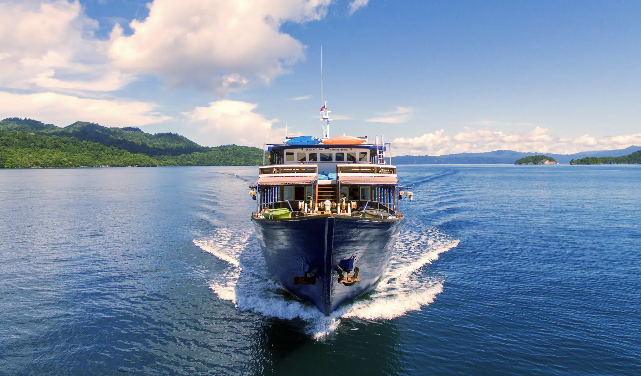 mv ambai cruising, deep blue water, green hills in the background, clear sky 