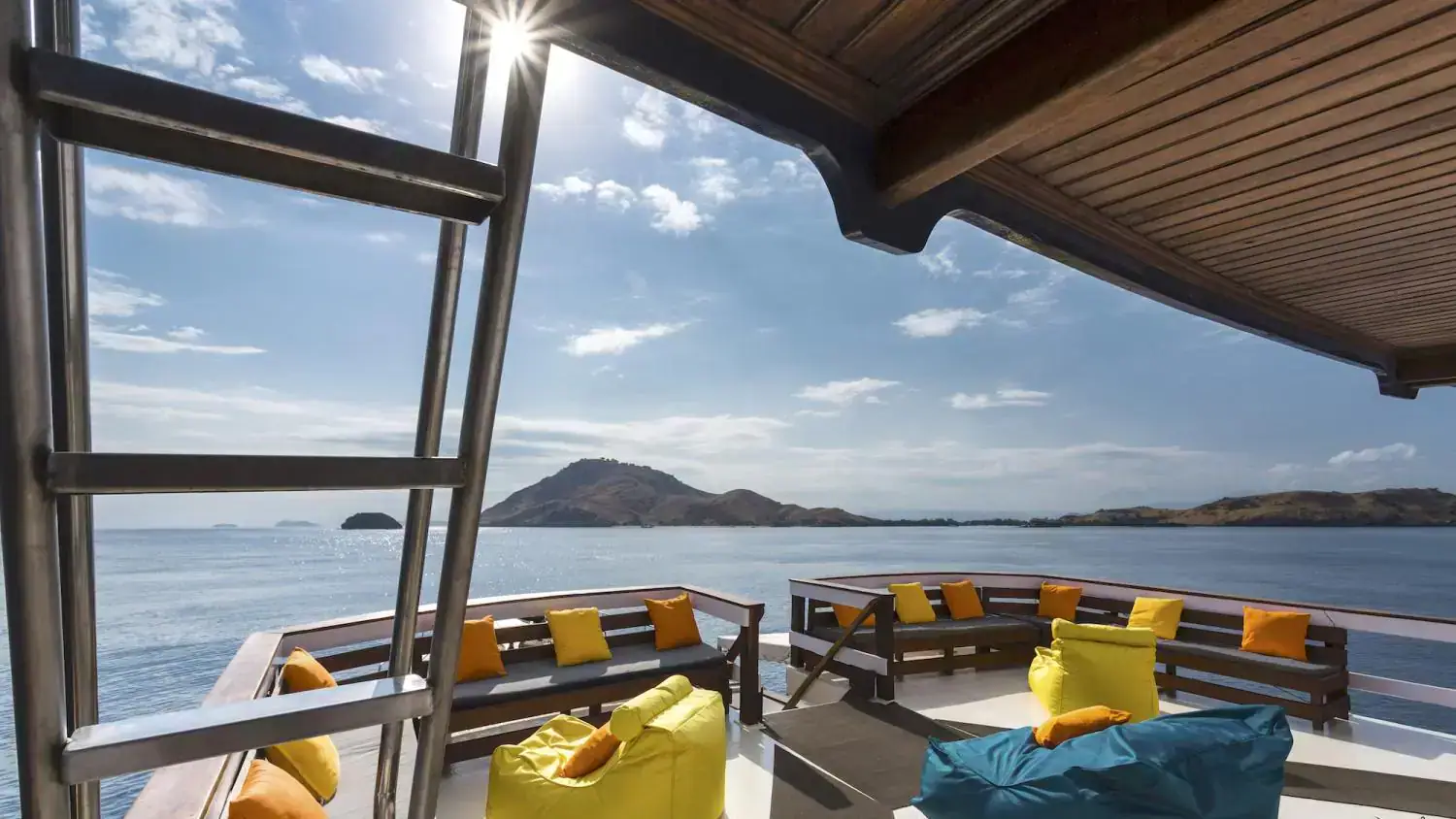 upper deck a, relaxing spot, yellow and orange pillows, wide view, hills in the background, yellow and blue ottomans, sunshine